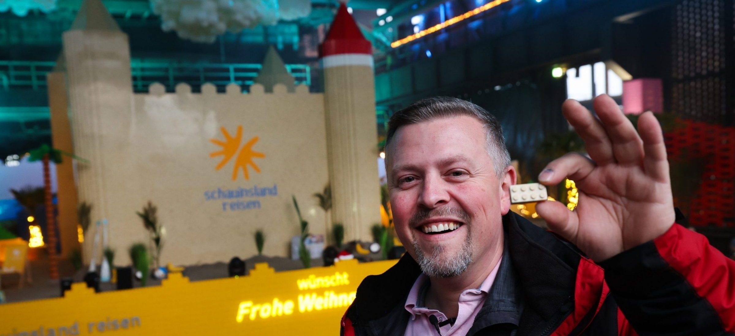 Adrian Kniewald steht mit einem LEGO Stein in der linken Hand vor der Weltrekord Sandburg aus LEGO Steinen in Duisburg auf dem Lichtermarkt.